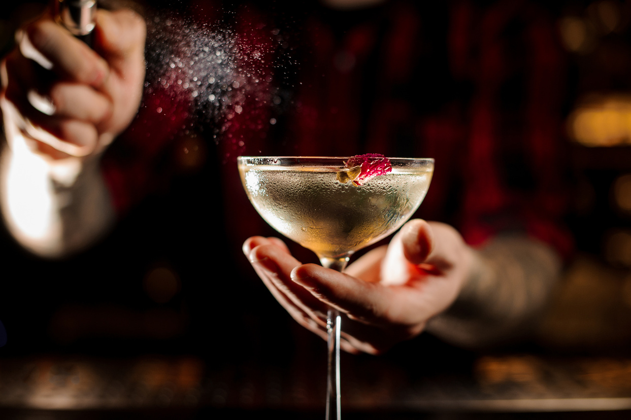 Mixologist sprinkling bitter on the elegant cocktail glass